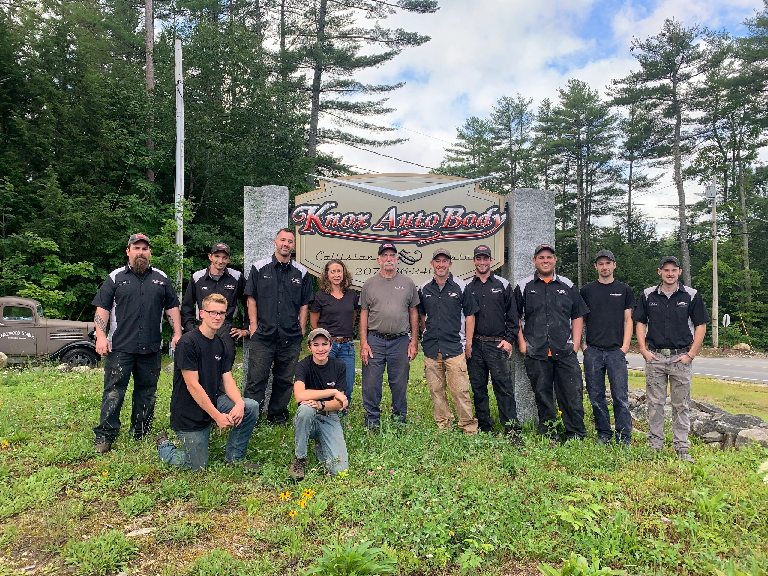 Knox Auto Body crew in front of the shop's roadside sign